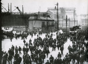 Treballadors sortint de les drassanes de Harland, el 1911, amb el Titanic al fons.